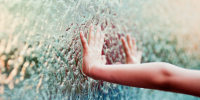 Kinderhand berührt Wasser, das an der Glaswand fließt.