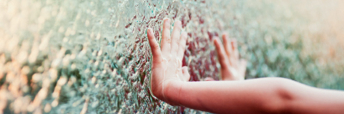 Child's hand touching water flowing on glass wall.