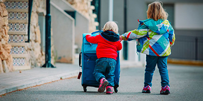 zwei kleine Kinder schieben auf einer Straße einen Koffer, Ansicht von hinten